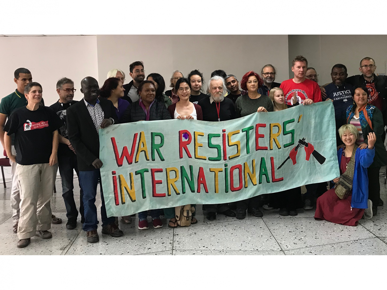 Two dozen people stand behind a banner reading "War Resisters' International"
