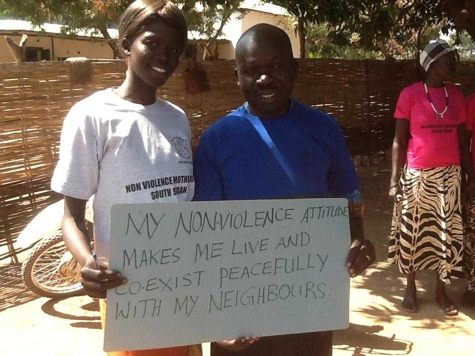 Activists hold a sign saying "My nonviolence attitude makes me live peacefully and coexist with me neighbours"