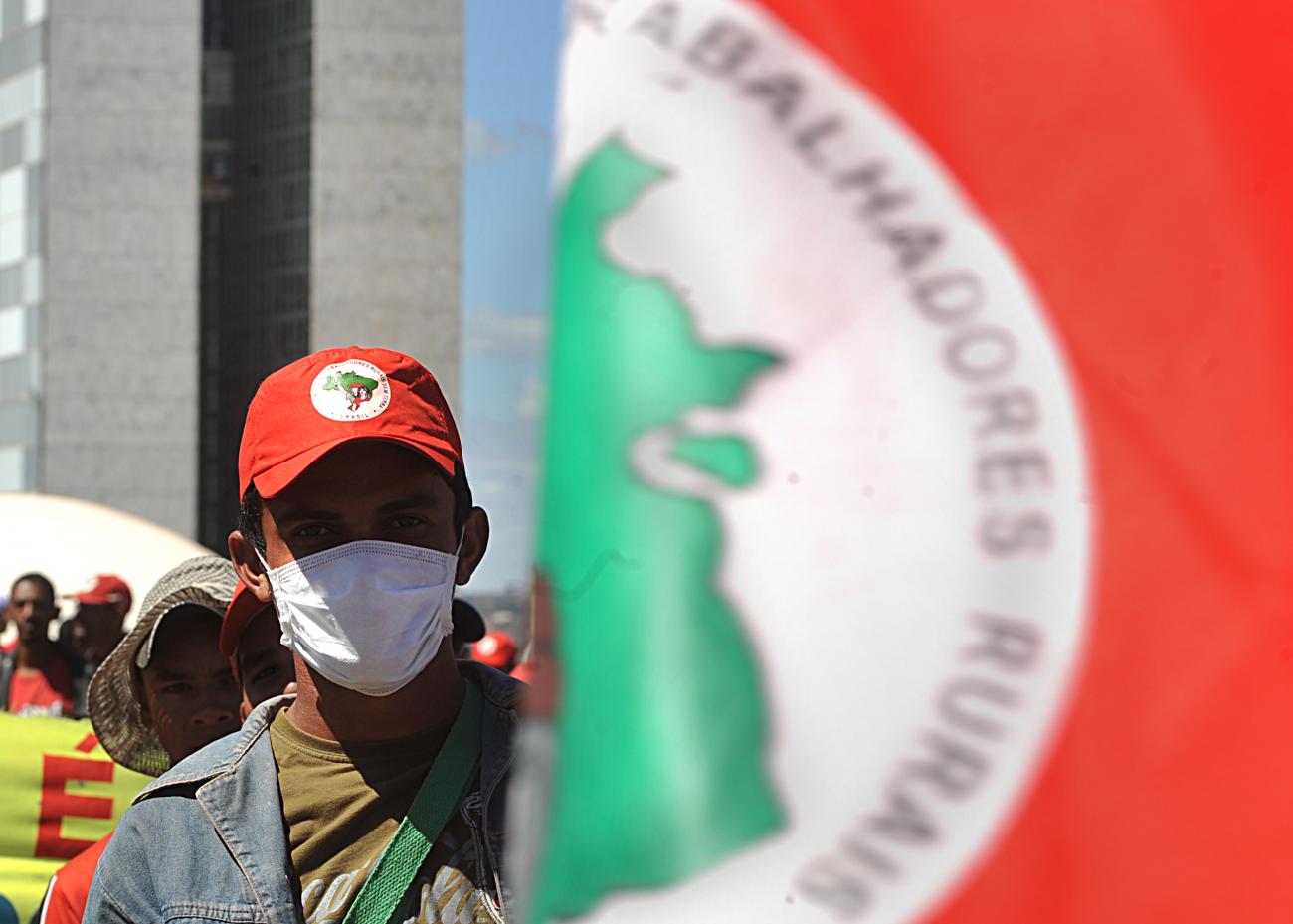 A man wears a mask while stood next beyind a red, green and white MST flag
