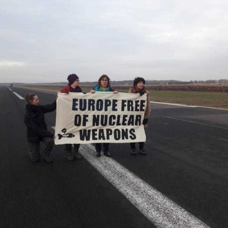 Four activists stand in a runway with a banner reading "Europe free of Nuclear Weapons"