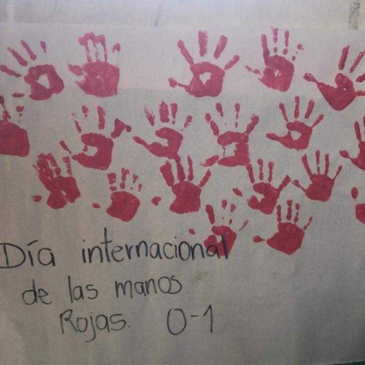 A sign covered in red hands reads "International red hand day" in Spanish