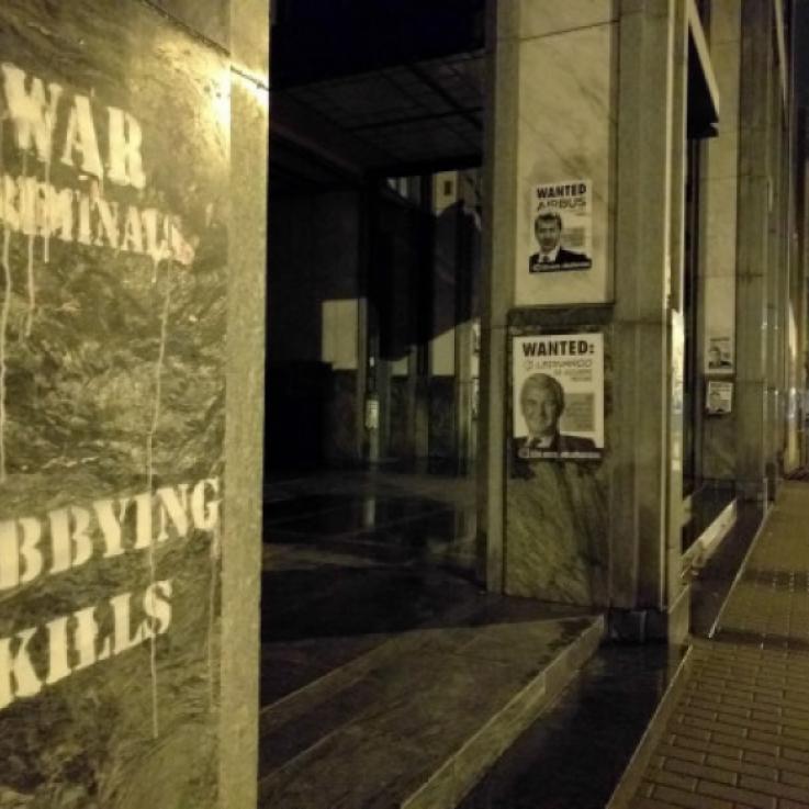 Image taken at night. Grafitti saying "Lobbying kills" and "war criminals" alongside a Wanted poster