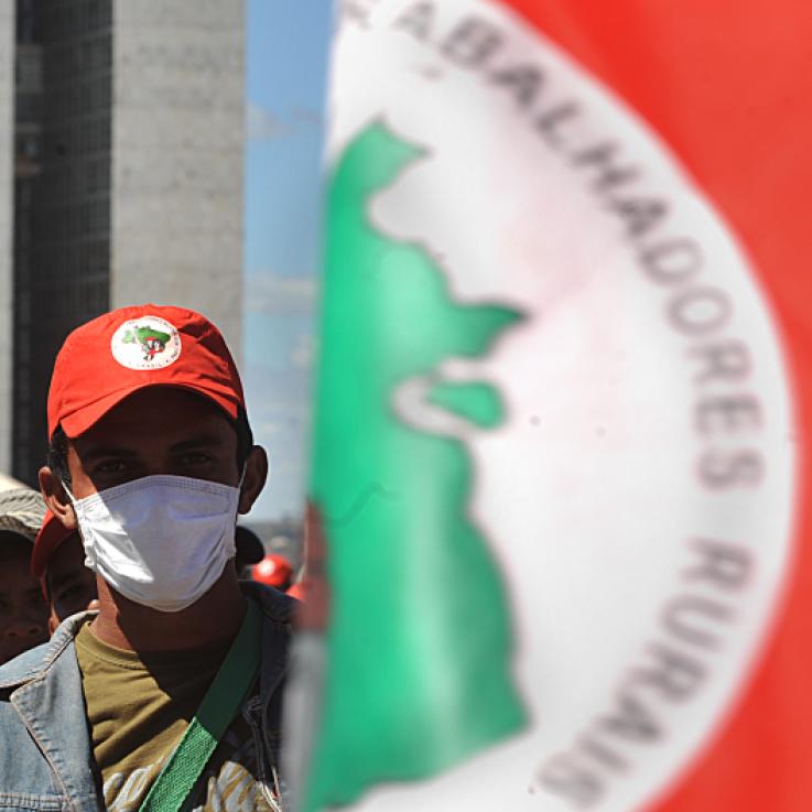 A man weUn hombre lleva una máscara mientras está de pie junto a una bandera roja, verde y blanca del MST.ars a mask while stood next beyind a red, green and white MST flag