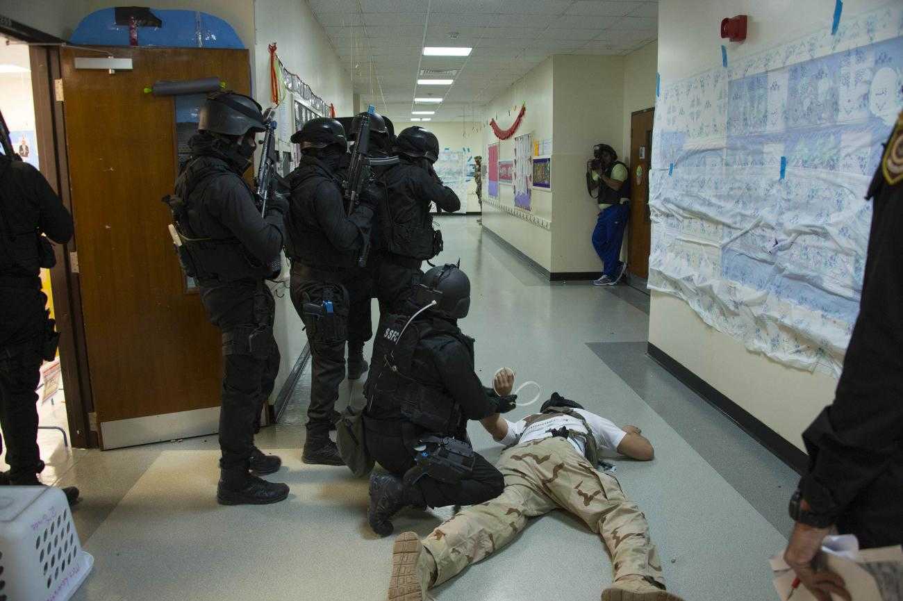 A training exercise involving Bahraini and US police. A man being "arrested" is held to the floor while others point guns down a corridor. There is a photographer in the background.