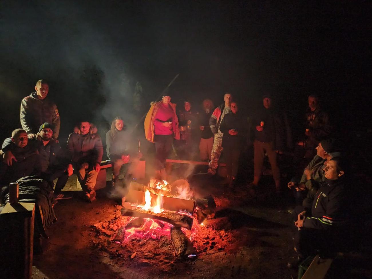 A large group of people sitting around a campfire at night