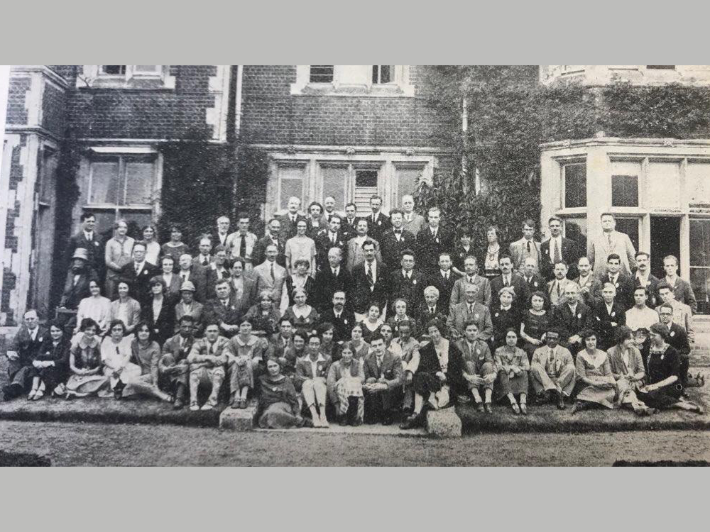 A black and white photo showing many people sat outside in front of an old building
