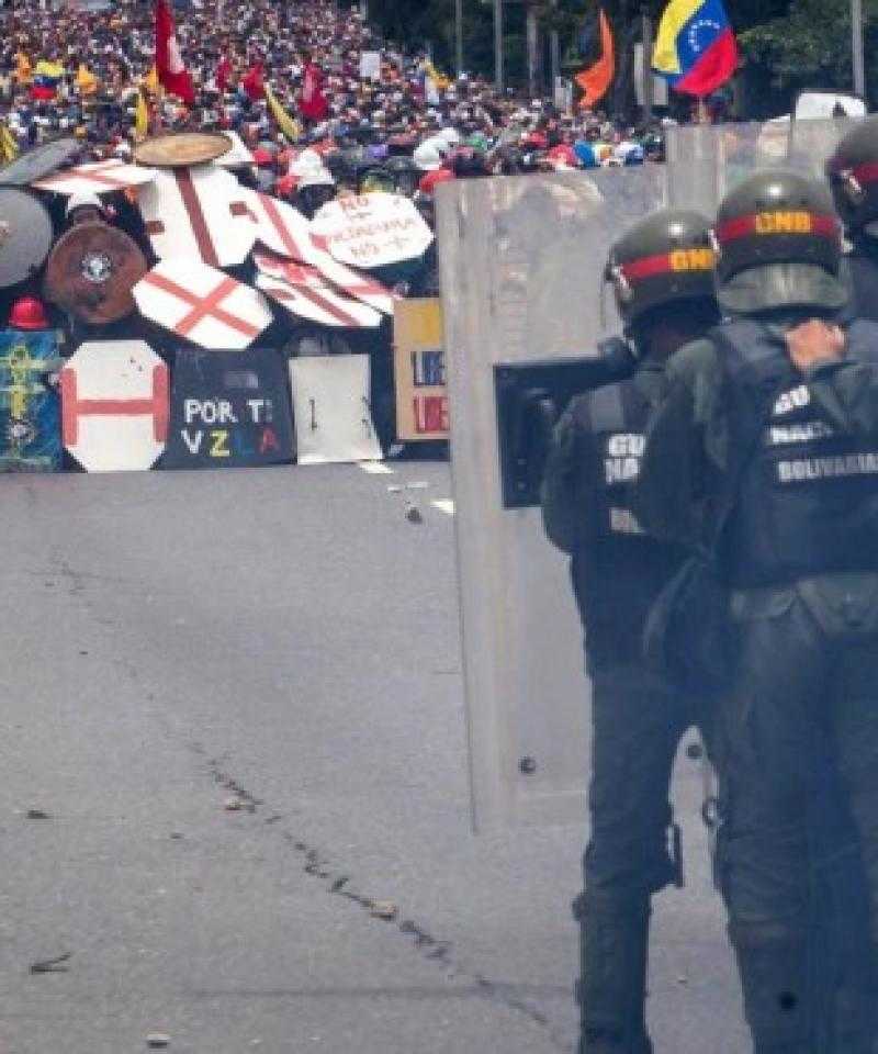 Police behind riot shields face a crowd of protesters behind a wall of homemade shields in Venezuela