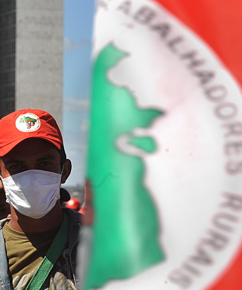 A man wears a mask while stood next beyind a red, green and white MST flag