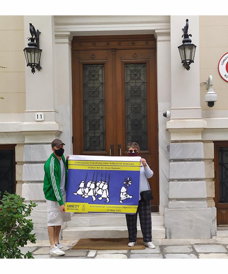 Dos personas sosteniendo una pancarta frente a un edificio