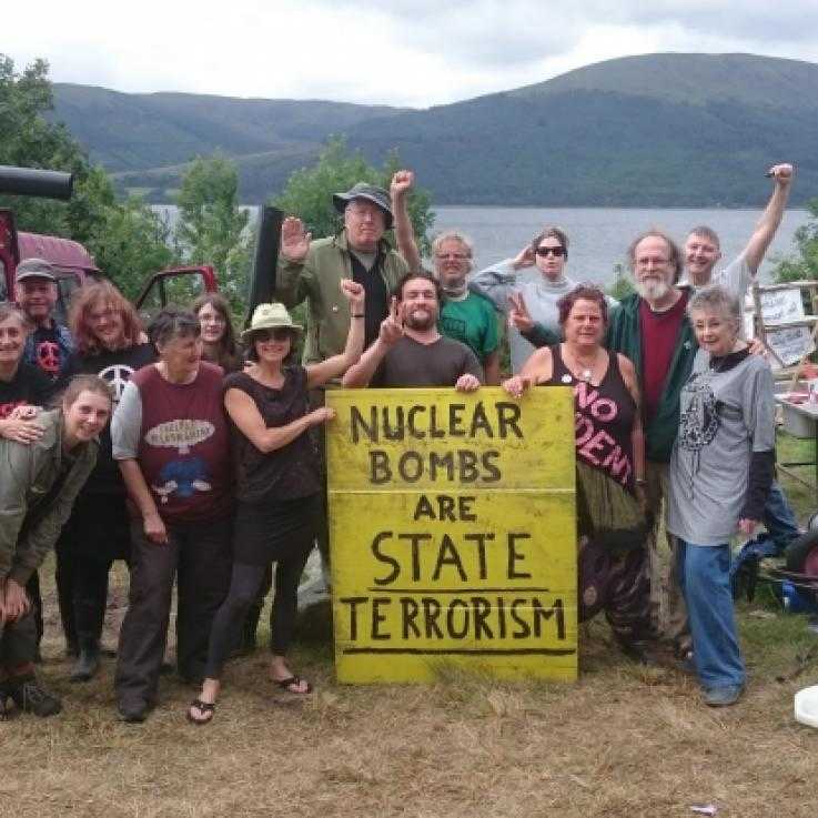 Gathering of people at the Coulport Disarmamnet camp. People hold a banner saying 'Nuclear weapons are state terrorism'